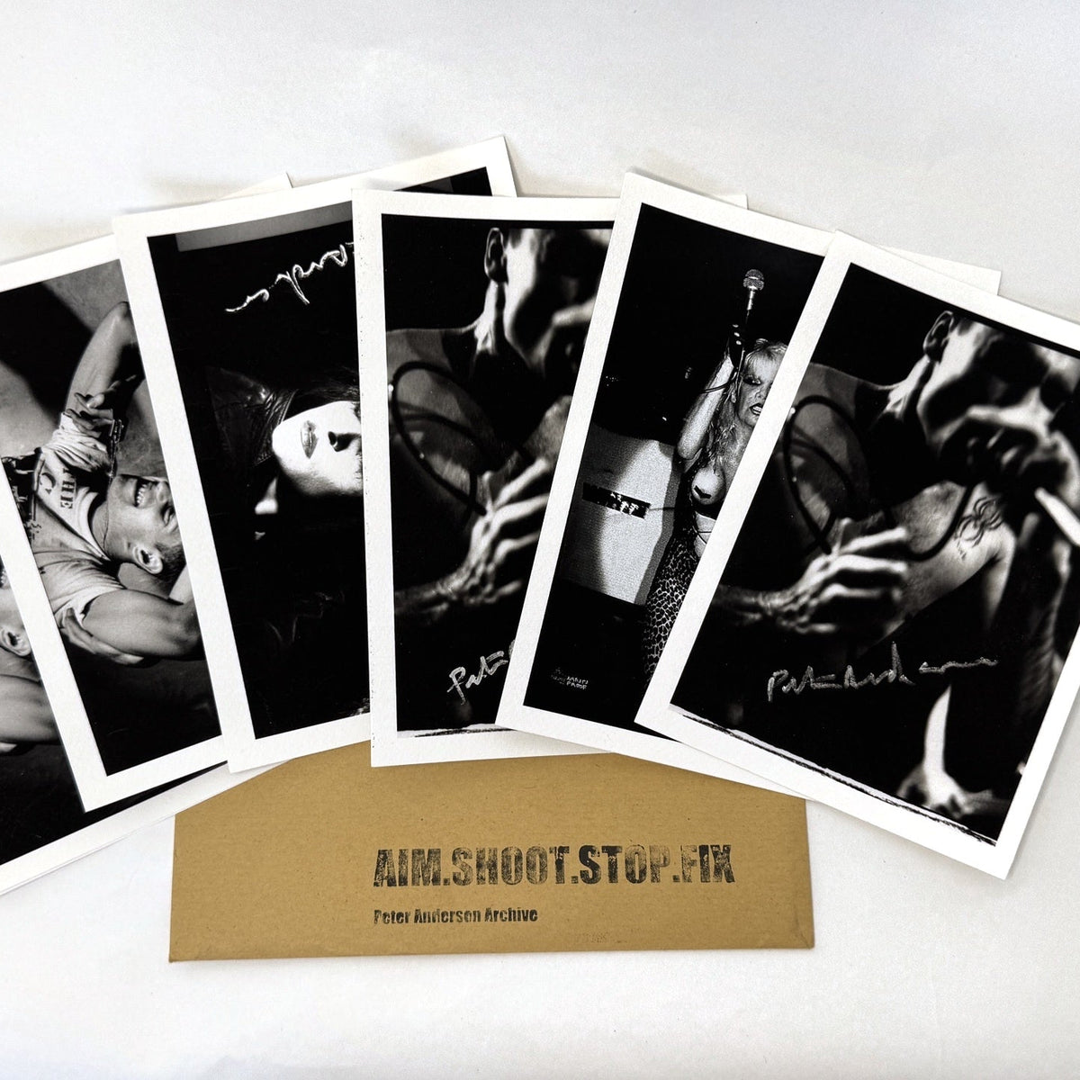 A set of five black and white photographic prints fanned out above a tan card labeled 'AIM/SHOOT STOP FIX' on a plain white background.