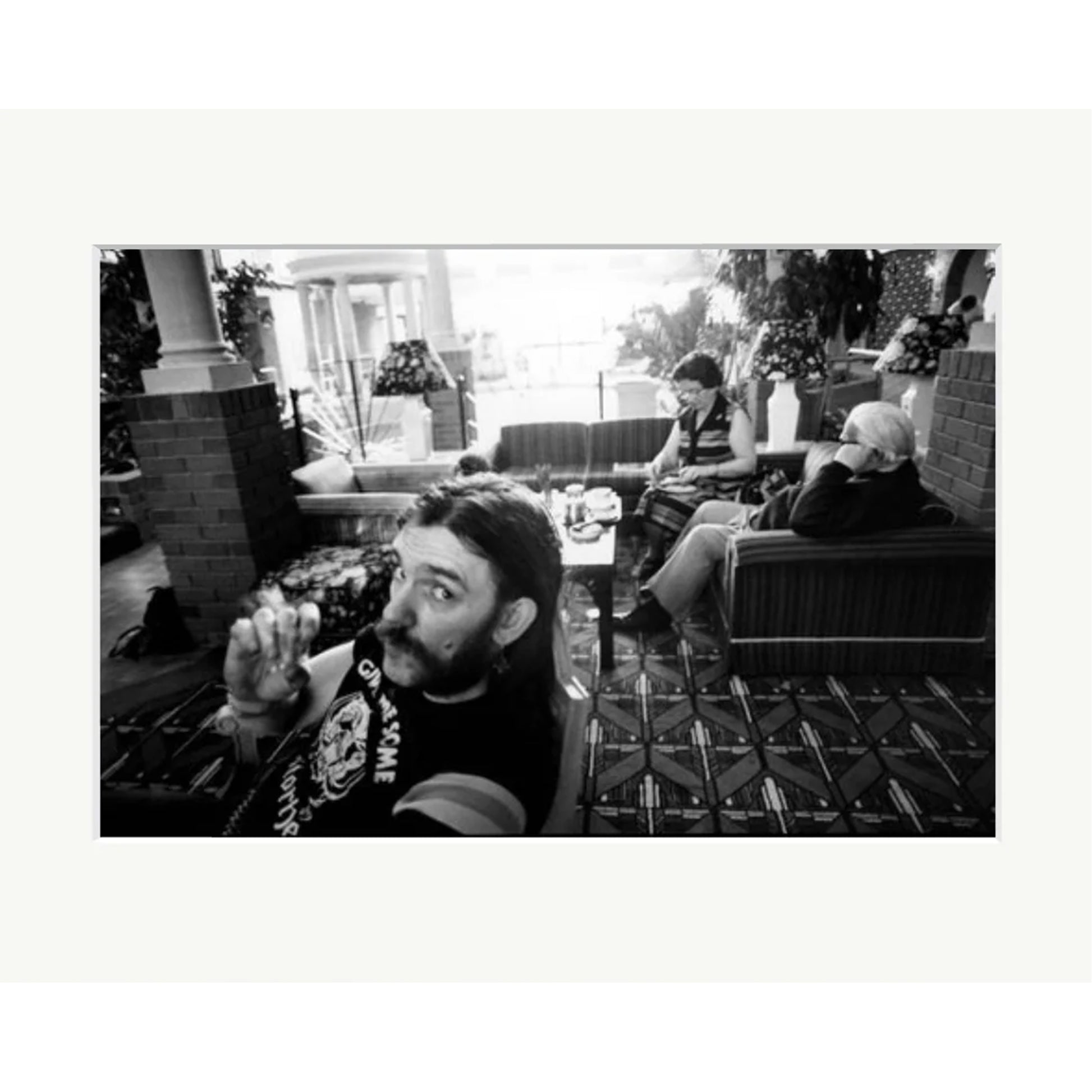 Silver gelatin darkroom print of Lemmy Kilmister from Motörhead, captured by Peter Anderson during breakfast at a Portsmouth Holiday Inn, 1983. The black and white photograph shows Lemmy in the foreground of a hotel lobby with other guests in the background.